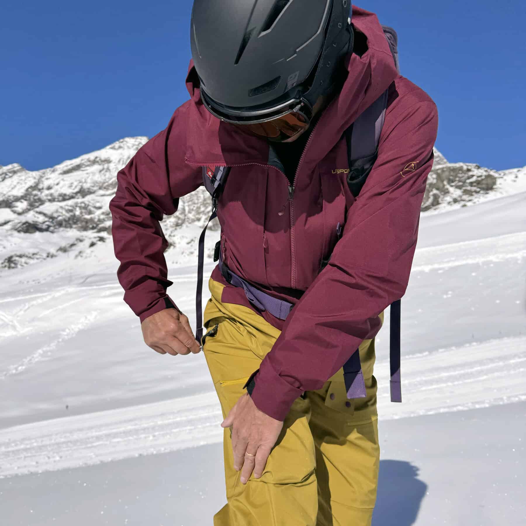 Layered outdoor mountaineering jacket in burgundy and yellow for winter sports and snow trekking.